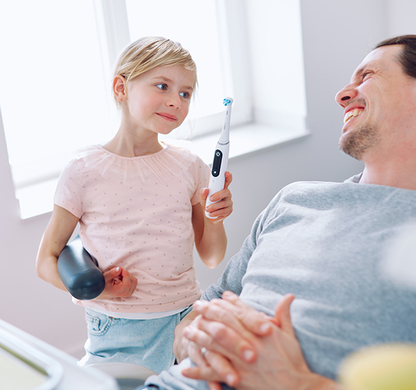 Mädchen zeigt lachendem liegendem Vater E-zahnbürste
